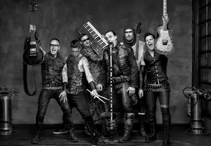 Zespół Rammstein, w tym Till Lindemann, gotowy do rockowego występu. W tle klawisze i gitary, jak w ich hicie "Radio".