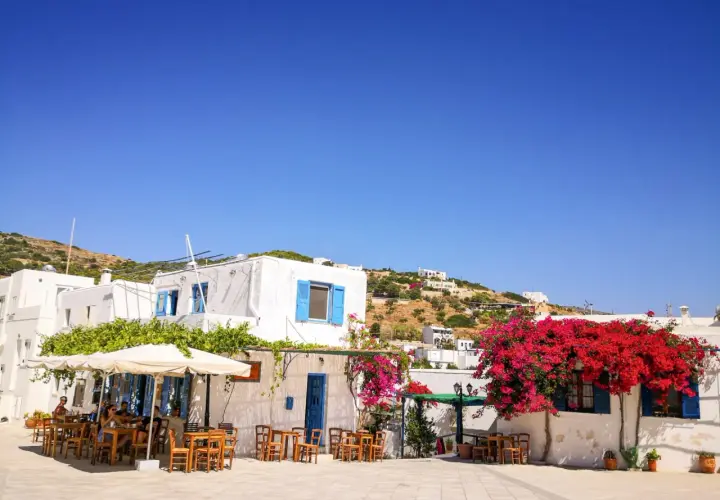 Un angolo di **Grecia con bambini** che giocano felici tra i tavolini di un caffè, sotto bouganville fiorite e il cielo azzurro.