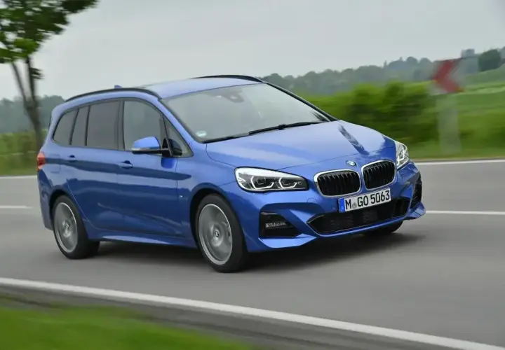 Niebieskie BMW 218i w wersji kombi pędzi po drodze, otoczone zielenią i drzewami.