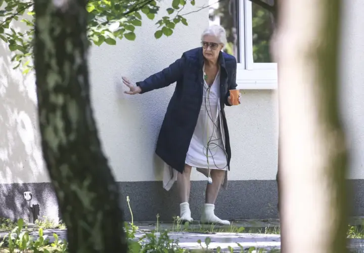 Beata Tyszkiewicz w domu opieki, z kubkiem w dłoni, oparta o ścianę.