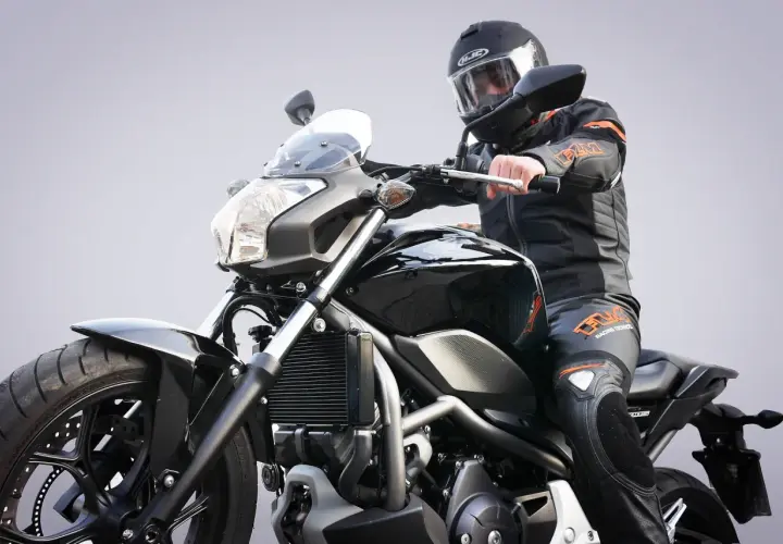 Motocykl od ilu lat? Młody motocyklista w czarnym kombinezonie i kasku na czarnym motocyklu.