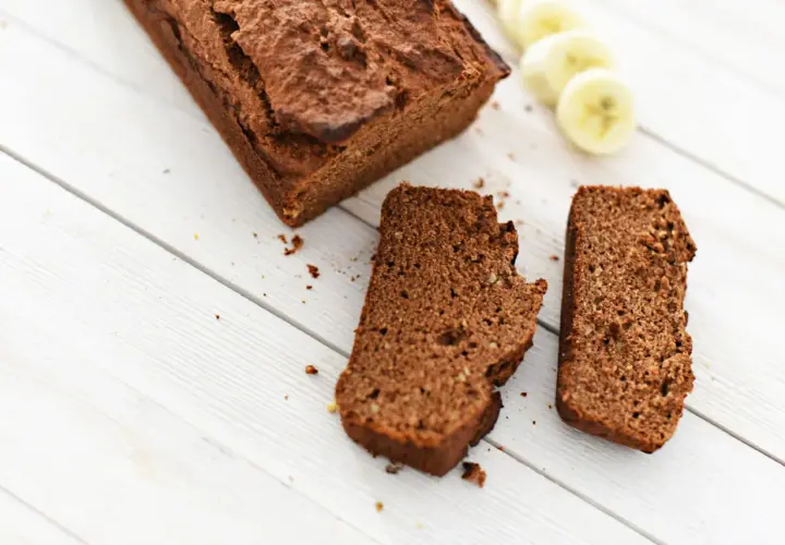 Chlebek bananowy Ani gotuje się na białych deskach. Obok leżą dwa kawałki ciasta i plasterki banana.