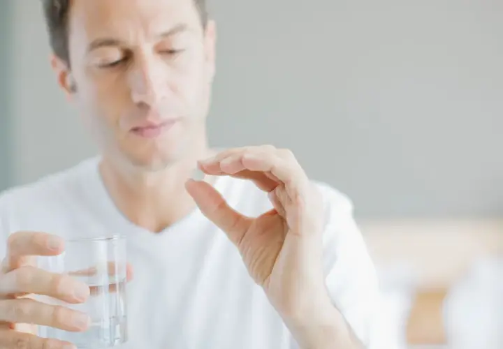 Mann hält Tablette und Glas Wasser, fragt sich, wie viel Magnesium bei Tinnitus hilft.