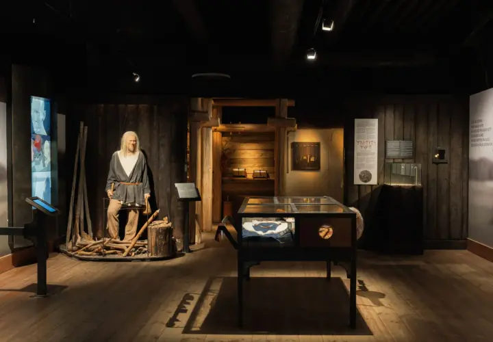 Vikingamuseum Stockholm: en vaxdocka av en viking med yxa, utställningsmontrar med föremål och informationstavlor.
