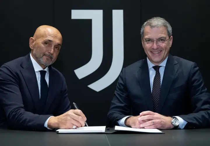 Dwóch mężczyzn w garniturach, prawdopodobnie trenerzy Juventusu, siedzi przy stole. Jeden z nich podpisuje dokumenty.