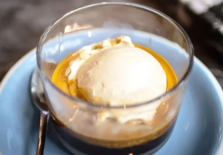 Pyszne affogato: gałka lodów waniliowych w gorącym espresso, podana w szklance na jasnoniebieskim talerzyku.