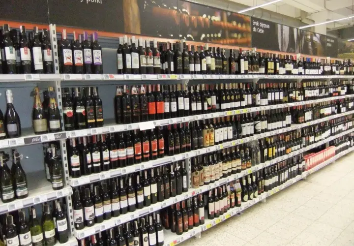 Rzędy butelek wina, w tym wino z suszonych winogron, na półkach sklepowych.