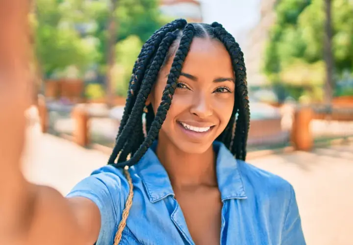 Sonrisa radiante de una mujer con distintos tipos de trenzas africanas, luciendo un estilo moderno y seguro.