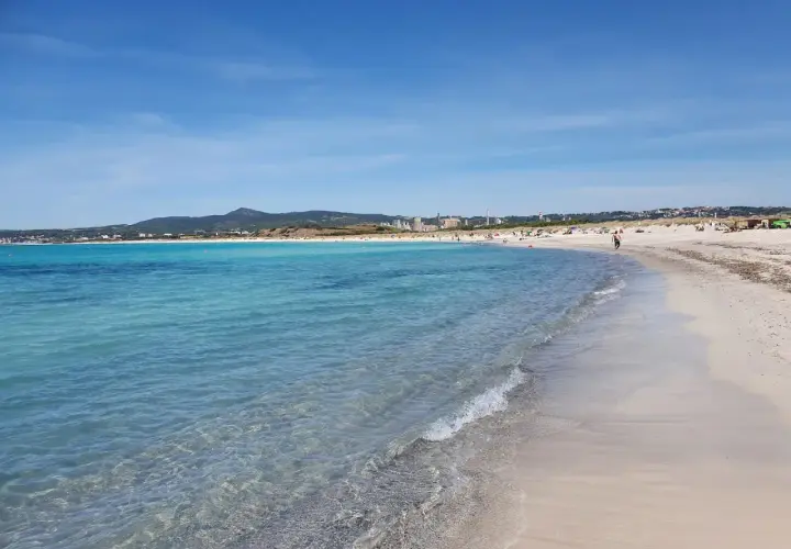 Plage de sable fin à Vada, eaux turquoise, ciel bleu, quelques personnes profitent du soleil.