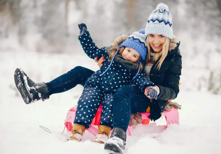 Radosne ferie zimowe 2026 lubelskie! Mama i córka na sankach, śmieją się w śnieżnym krajobrazie.