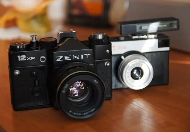 Dwa klasyczne aparaty na film: czarny Zenit 12XP i srebrno-czarny Smiena z lampą błyskową.