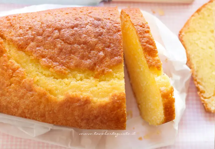 Un soffice plumcake allo yogurt, dorato e invitante, tagliato a fette su carta bianca.
