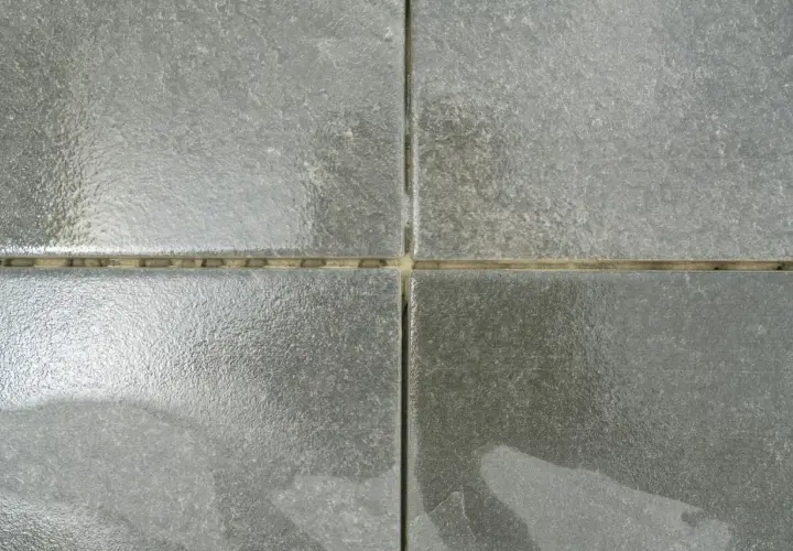 Dettaglio di quattro piastrelle grigie con fughe vuote, pronte per essere riempite. Una guida visiva su come riempire le fughe delle piastrelle.