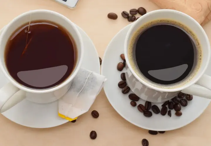 Zwei Tassen, eine mit schwarzem Tee und Teebeutel, die andere mit Kaffee und Kaffeebohnen. Perfekt, um Kaffee und Tee zusammen zu trinken.