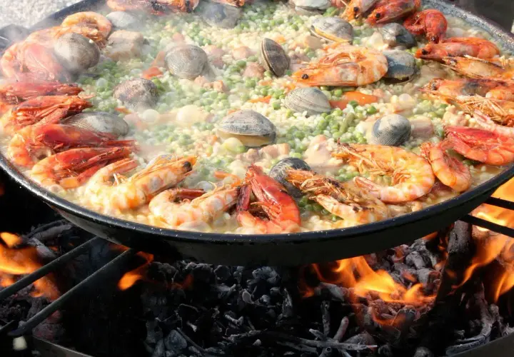 Gros plan sur une paella aux crevettes et palourdes, cuisant sur un feu de bois. Quel vin avec jambalaya ? Un blanc sec ou un rosé fruité serait parfait.