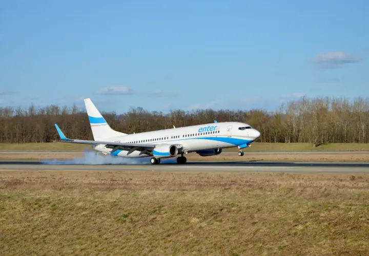 Samolot Enter Air ląduje na pasie startowym, unosząc kłęby dymu.