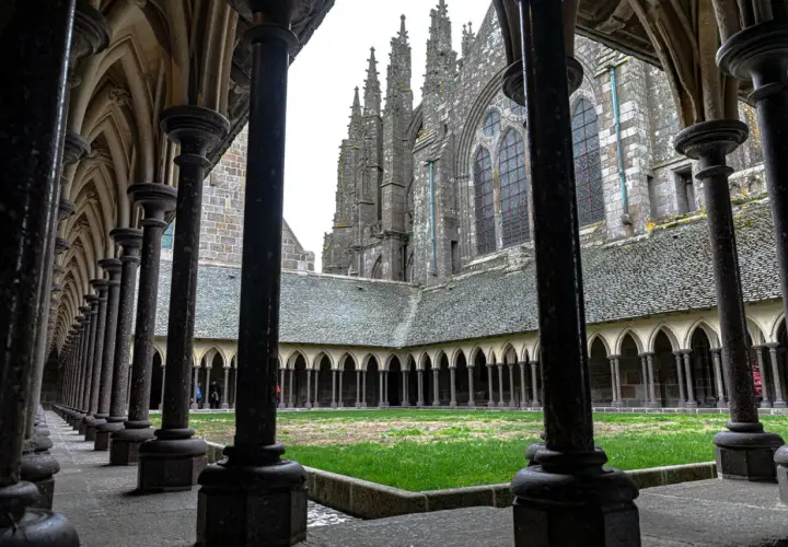 Ein Blick durch die Säulenhalle auf den Kreuzgang des Mont Saint Michel innen. Grüne Wiese und gotische Architektur.