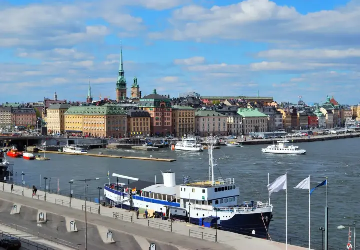 Widok na port w Sztokholmie, gdzie cumuje prom. W tle kolorowe kamienice i wieże.