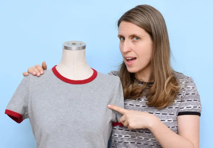 Woman points to a grey t-shirt on a mannequin, demonstrating how to sew a shirt.