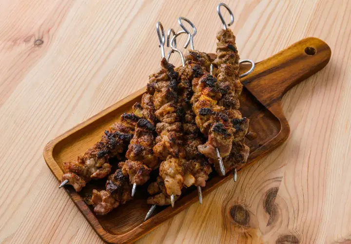 Cinq brochettes d'agneau grillées, savoureuses et légèrement caramélisées, reposent sur un plateau en bois.