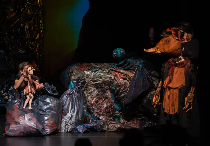 Na scenie teatru lalki i aktora w Łomży, dziewczynka animuje drewnianą lalkę, obok niej ptak i postać z głową zwierzęcia.