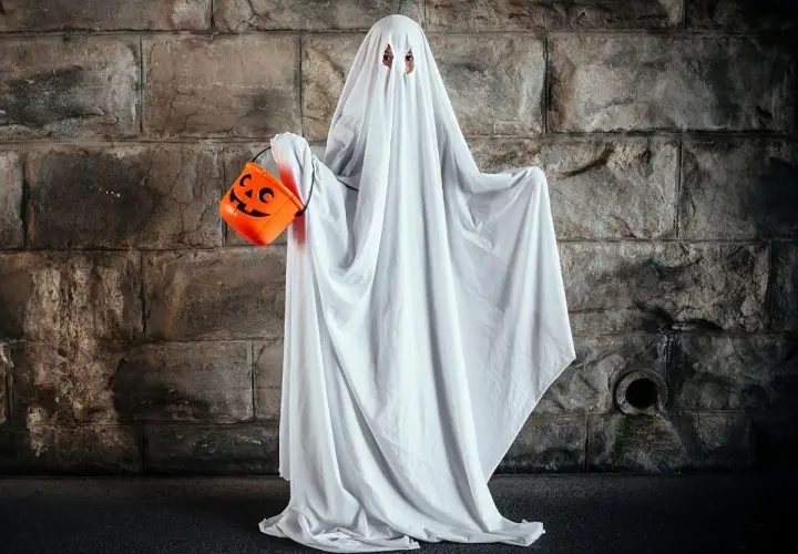Dziecko w przebraniu na Halloween DIY jako duch, trzymające pomarańczową dynię na cukierki.