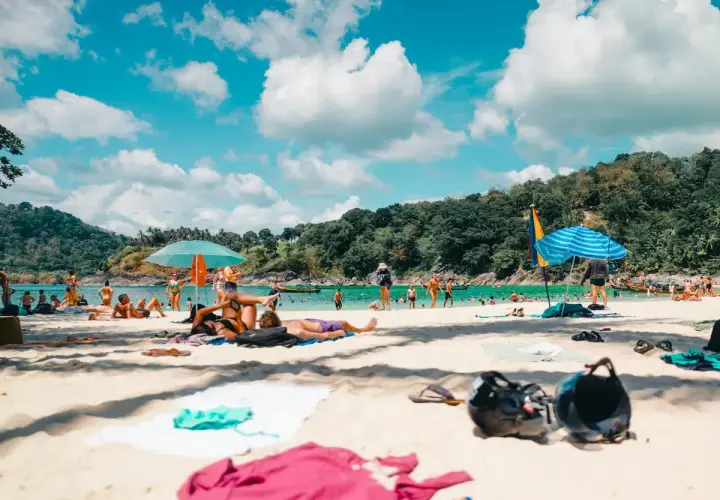 Gente disfrutando de unas **vacaciones agosto 2026** en una playa tropical, con aguas turquesas y vegetación exuberante.