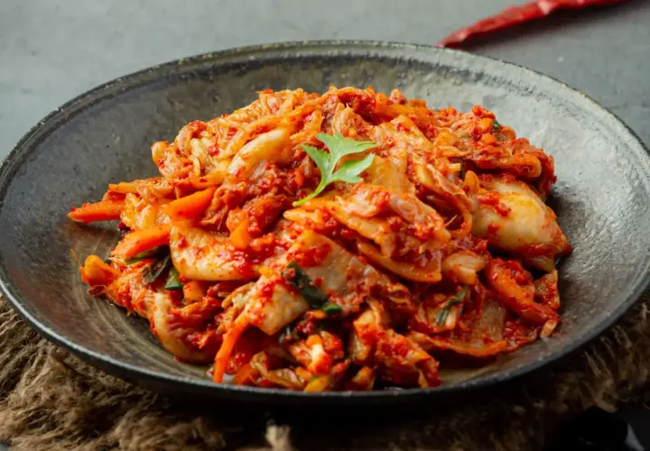 Miseczka z pikantnym kimchi, ozdobiona listkiem kolendry.