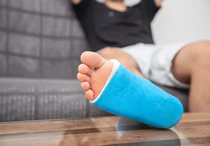 Niebieski gips na nodze, która odczuwa ból kostki po wewnętrznej stronie.