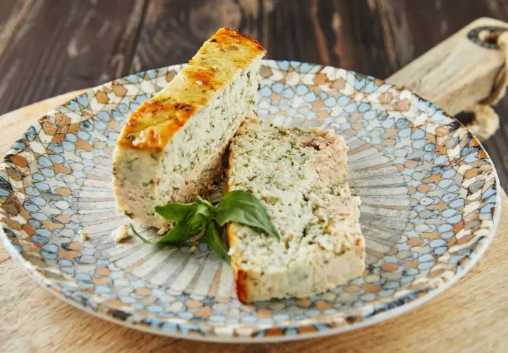 Deux tranches de terrine de poisson aux herbes, garnies d'une feuille de basilic, sur une assiette décorée.