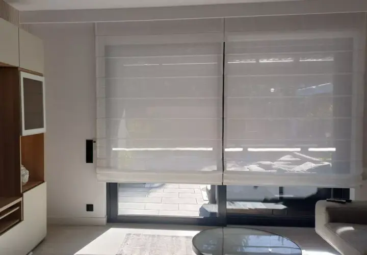 Eleganckie rolety elektryczne wewnętrzne na baterie, wykonane z półprzezroczystego materiału, tworzą przytulną atmosferę w nowoczesnym salonie.