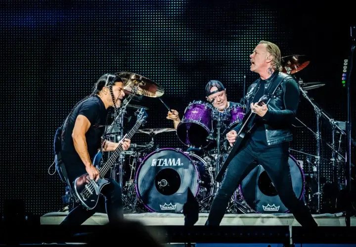 Duński zespół rockowy na scenie: basista z warkoczami, perkusista w fioletowym zestawie i gitarzysta w skórzanej kurtce.