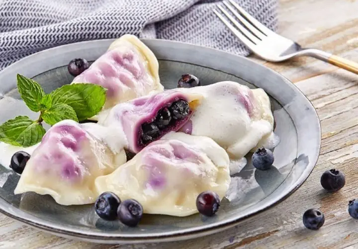 Pyszne pierogi z jagodami, polane śmietaną, ozdobione miętą i świeżymi owocami. Idealne na deser!