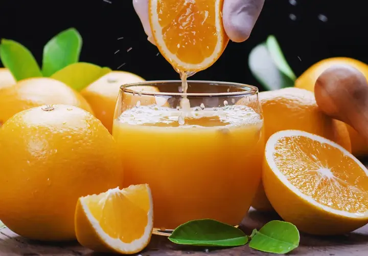 Un vaso de zumo de naranja recién exprimido, rodeado de naranjas frescas. ¡Cuidado! el zumo de naranja engorda si se abusa de él.