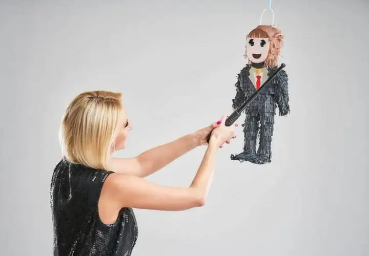 Une femme en robe à paillettes s'apprête à frapper une piñata en forme d'homme en costume, symbole d'une fête de divorce réussie.