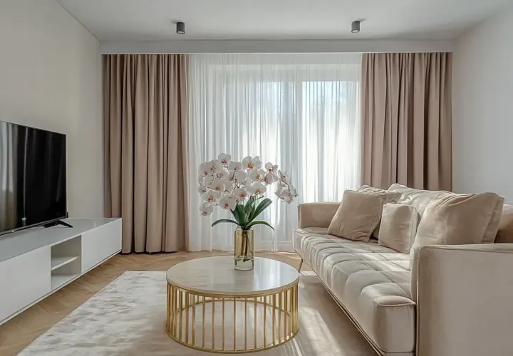 Elegancki salon z zasłonami na karniszu sufitowym z maskownicą, jasną kanapą i stolikiem kawowym.