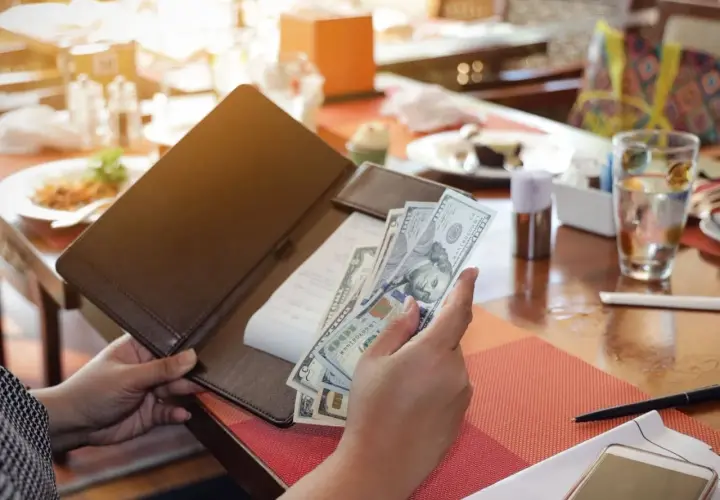 Rachunek w restauracji, ręka trzyma banknoty dolarowe. Poproszę rachunek po angielsku.