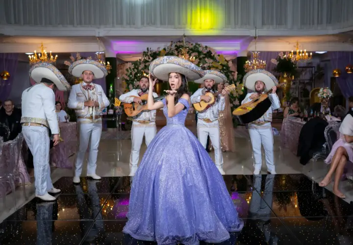 Mariachi grają przyśpiewki weselne, a młoda kobieta w fioletowej sukni posyła całusy.