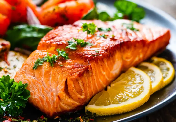 Un succulento filetto di salmone cotto alla perfezione, guarnito con prezzemolo fresco e accompagnato da spicchi di limone e pomodorini.
