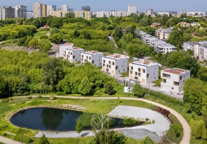Nowoczesne domy w otoczeniu zieleni, z widokiem na miasto. Widać tu staw i ścieżki spacerowe, idealne do odpoczynku. To miejsce, gdzie życie w stylu sikorskiego vita jest możliwe.