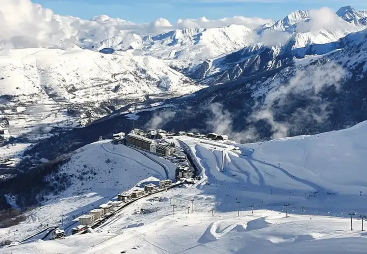 Vista aérea de Saint Lary Soulan, un pueblo de montaña cubierto de nieve con edificios y pistas de esquí, rodeado de majestuosas montañas nevadas.