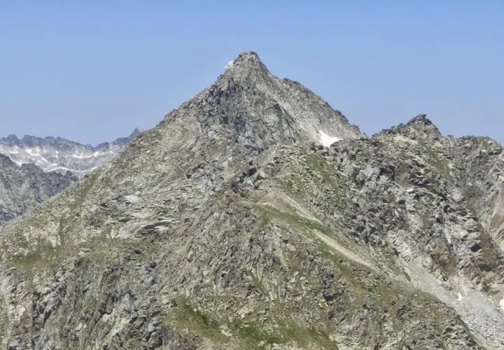 Majestuoso pic de peguera rocoso y escarpado, con nieve en sus cumbres y un cielo azul despejado.