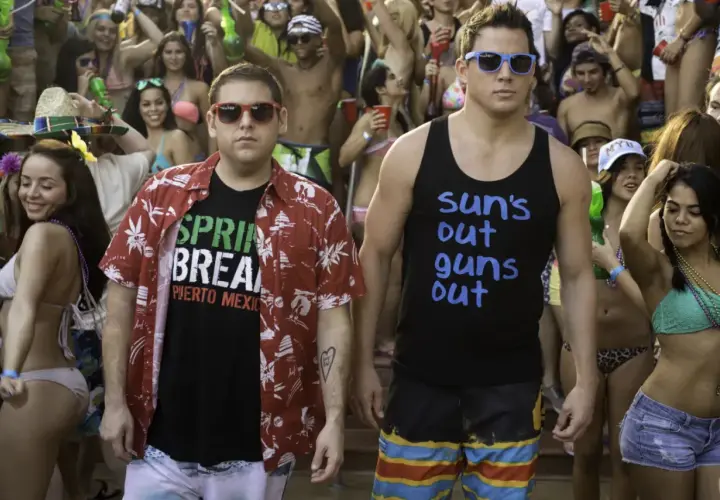 Dwóch facetów w okularach przeciwsłonecznych, jeden w koszulce "Spring Break Puerto Mexico", drugi w "Sun's out guns out", na imprezie w stylu jump street 23.