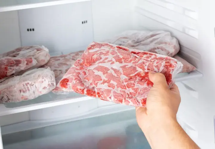 Ręka wyjmuje z zamrażarki paczkę mrożonej surowej karkówki. Dowiedz się, jak długo można mrozić surową karkówkę, żeby nie zjełczał w niej tłuszcz.