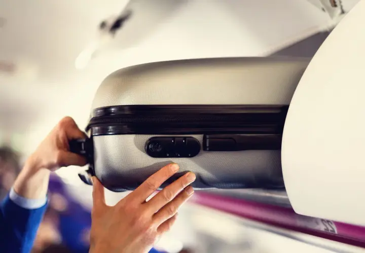 Ręce wkładają srebrną walizkę do schowka nad głową w samolocie. Czas na podróż z Malta Air!