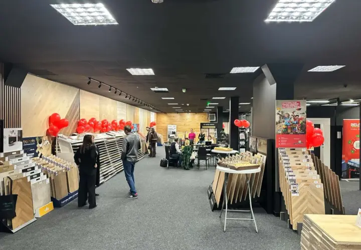 Wnętrze salonu z wystawionymi panelami podłogowymi, dekoracjami z balonów i ludźmi.