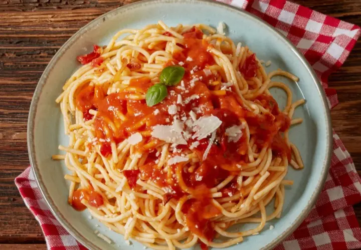 Spaghetti z sosem pomidorowym, parmezanem i bazylią na talerzu.