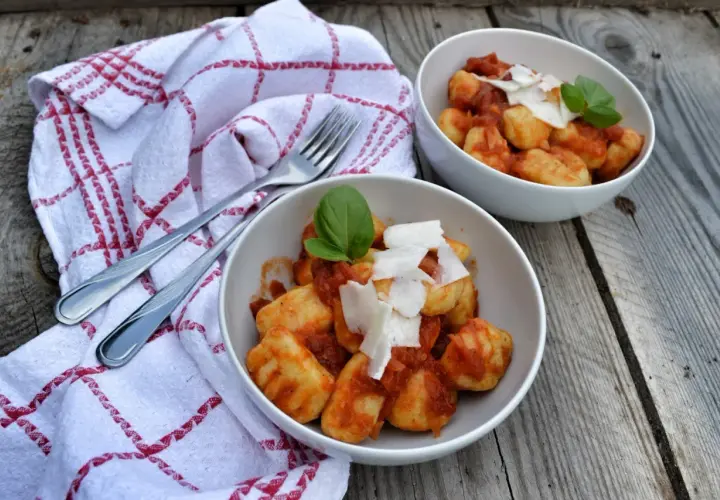 Dwa talerze pysznych gnocchi z sosem pomidorowym, posypane parmezanem i udekorowane bazylią, gotowe do podania.