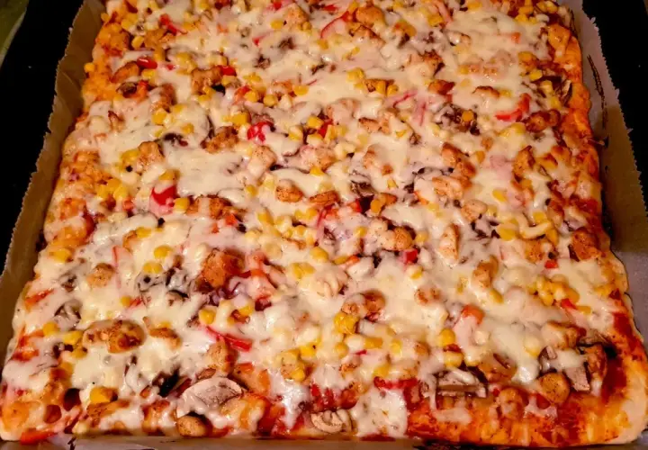 Prostokątna pizza z kurczakiem, kukurydzą, papryką i serem.