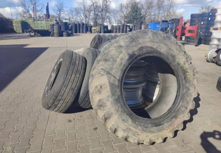 Duże opony rolnicze i samochodowe czekają na recykling opon. W tle widać stosy opon i sprzęt.